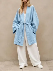 Full-length view of a women's loose light blue belted cardigan jacket with white pants.