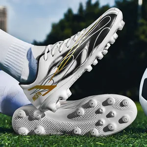 Crampons de football blancs avec motifs de flammes noir et or sur un terrain d'herbe