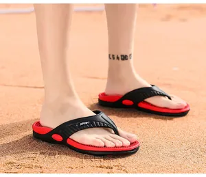Primo piano di comode infradito da massaggio nere e rosse da uomo su una spiaggia di sabbia