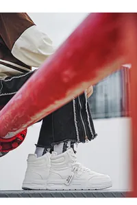 Dettaglio laterale di sneakers bianche alte indossate con jeans neri sfrangiati.