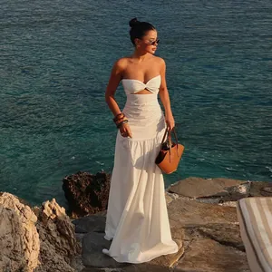 Elegant white strapless cutout maxi dress worn by a model standing on seaside rocks