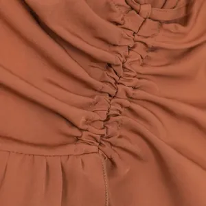Primer plano del sofisticado detalle fruncido en esta elegante falda midi color terracota