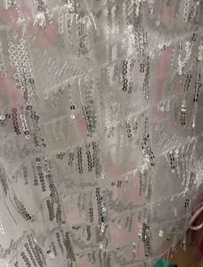 Gros plan sur un tissu en maille blanche avec des franges de paillettes argentées.