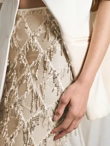 Vue détaillée de la broderie à pompons à paillettes sur une jupe en maille beige