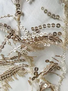 Détail macro de paillettes or champagne et franges sur un tissu en maille ivoire fin