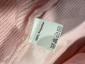 Detail van het waslabel op een roze gebreide trui van 100% polyester