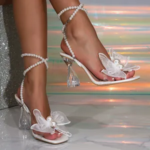 Detalle de sandalias blancas con lazo de tul, perlas y tacón grueso de cristal