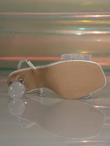 Vista detallada de sandalia blanca elegante con cadena de perlas y tacón de cristal