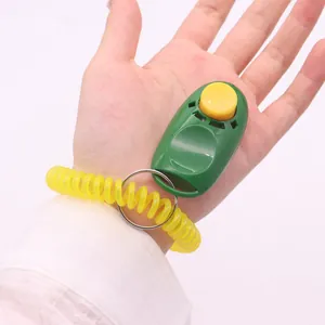 Portable green dog training clicker with yellow button and elastic wrist strap held in hand