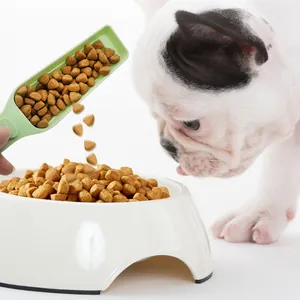 Green pet food scoop with sealing clip pouring kibble into a white bowl for a French bulldog