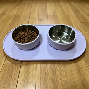 Light purple silicone pet feeding mat with two stainless steel bowls on wood floor.