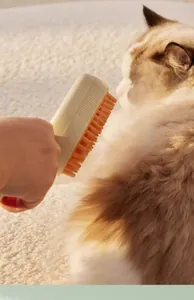 Gros plan d'une brosse de toilettage beige et orange peignant les poils d'un chat.