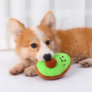 Ένας χαριτωμένος σκύλος Corgi που δαγκώνει ένα μαλακό λούτρινο αβοκάντο παιχνίδι