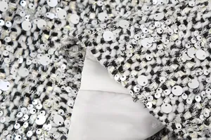 Close-up detail of black and white tweed fabric with silver sequins and white lining