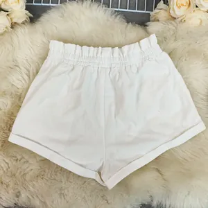 Close-up view of white cotton linen shorts on a fluffy rug, showing ruffled waist detail.