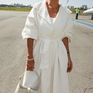 Detail van een elegante witte trenchcoat met lange mouwen en riem voor dames op een luchthaven