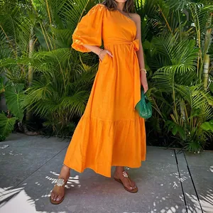 Detail view of a vibrant orange one-shoulder cotton linen maxi dress in a tropical setting