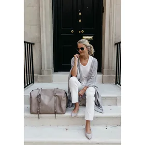 Chic blonde woman wearing grey loose knit cardigan while sitting on white stone steps outdoors