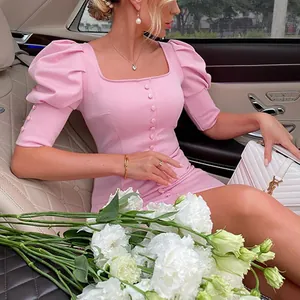 Elegant pink square neck dress with puff sleeves and button detail in a luxury setting.