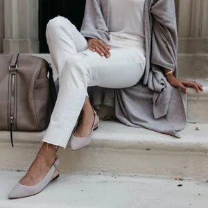 Detail view of a long grey knit cardigan with irregular hem styled with white jeans