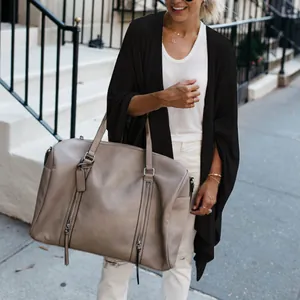 Detail view of a black knit cardigan with an irregular hem styled with a beige bag