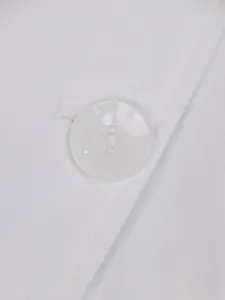 Macrodetail van een witte knoop op een minimalistische effen trenchcoat jas.