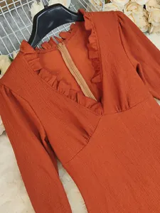 Detailweergave van de getextureerde stof en ruches V-hals van een oranje jurk met lange mouwen