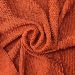 Dichtbij van de oranje getextureerde stof voor een effen maxi-jurk met lange mouwen.