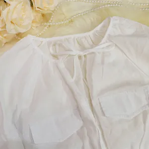 Detail view of a white cotton linen jumpsuit featuring a neck tie and twin pockets
