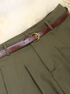 Close-up detail of olive green high-waisted trousers with a classic brown leather belt.