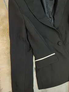 Detail view of a black blazer jacket with a sophisticated white trim on the pocket flap