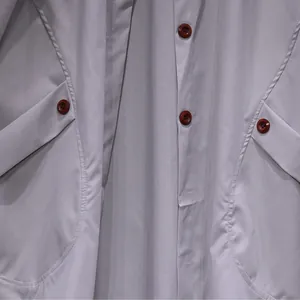 Close-up detail of a light gray women's trench coat featuring red buttons and pockets.