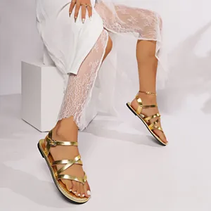 Close-up detail shot of gold metallic cross-strap flat gladiator sandals on a model