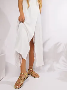 Close-up of gold cross-strap Roman flat sandals worn with a white lace dress.