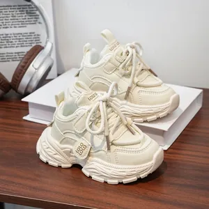 Vue de côté des baskets volumineuses pour enfants crème sur un fond de livre blanc.