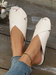 Elegant beige criss-cross closed-toe flat mule slippers shown on feet with a gold anklet.