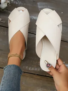 Detailed view of elegant off-white crossover strap flat mule slippers on wooden floor.