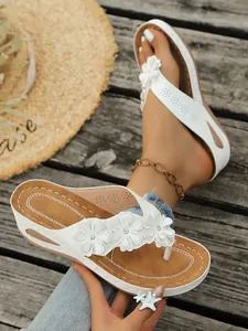 Detailweergave van witte wedge slippers met elegant bloemendecor op een houten dek
