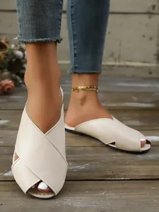 Detail view of stylish beige leather cross-strap flat mule slippers on rustic wood floor