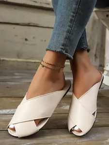 Detail shot of beige cross-strap flat mules on feet against a wooden background