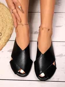 High-quality close-up detail of black faux leather peep-toe flat mule sandals on wooden floor
