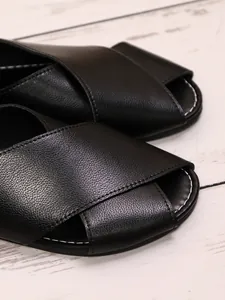 Detailed macro view of black textured leather cross strap sandals with stitching