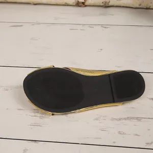 Close-up detail of the black non-slip outsole of a gold flat mule slipper for women