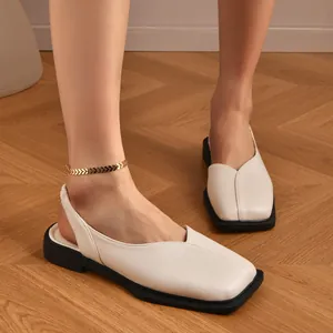 Dettaglio di sandali slingback beige a punta quadrata indossati su un pavimento in legno.
