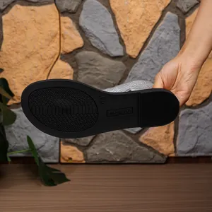 Detailansicht der rutschfesten schwarzen Sohle silberner flacher Damen-Römersandalen.