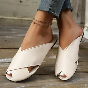 Elegant women's beige flat mule slippers with crossover straps on a rustic wooden deck