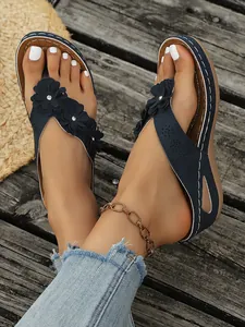 Detailopname van marineblauwe wedge slippers met bloemen en wit stiksel.