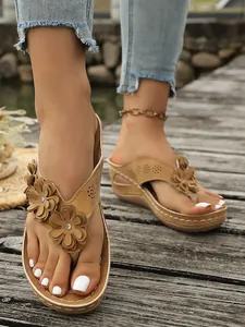 Detailopname van bruine teenslippers met sleehak, bloemaccenten en strass-steentjes