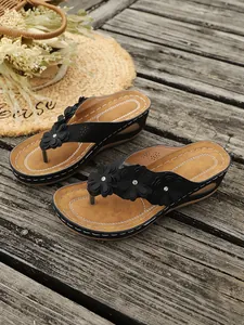 Detailopname van zwarte sleehak slippers met elegante bloemen en bruin voetbed