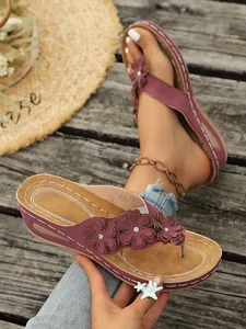 Detail van bordeauxrode wedge-slippers met bloemen en strass-accenten